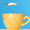 Spoon pouring sugar into yellow coffee cup on blue background