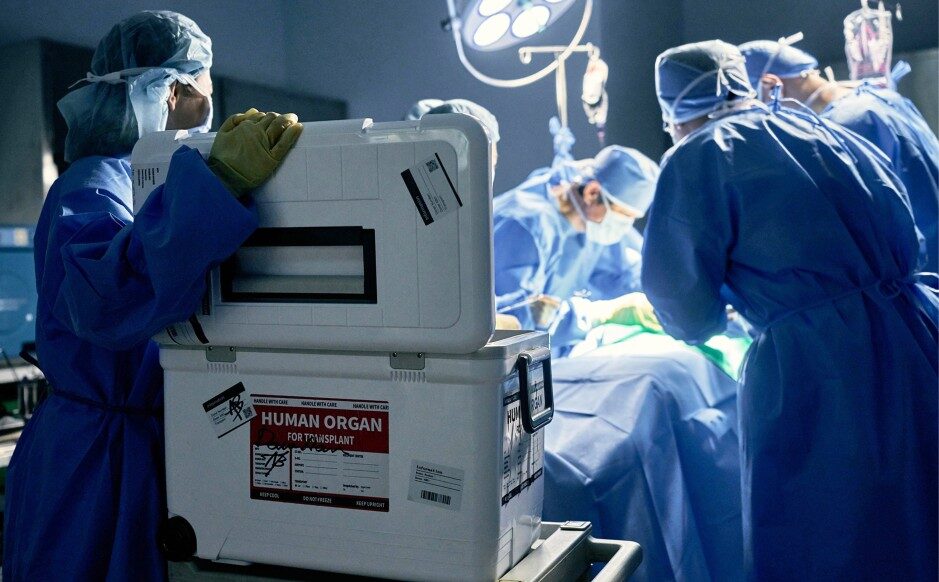 Doctors in operating room performing surgery with open cooler labeled human organ for transplant