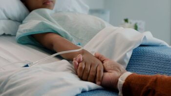 Adult holding sick child's hand in hospital bed