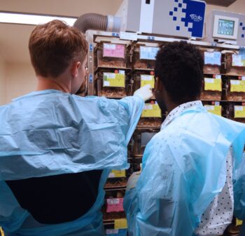 An animal care technician explains the cage card system to a visitor during a tour of the animal care facility.