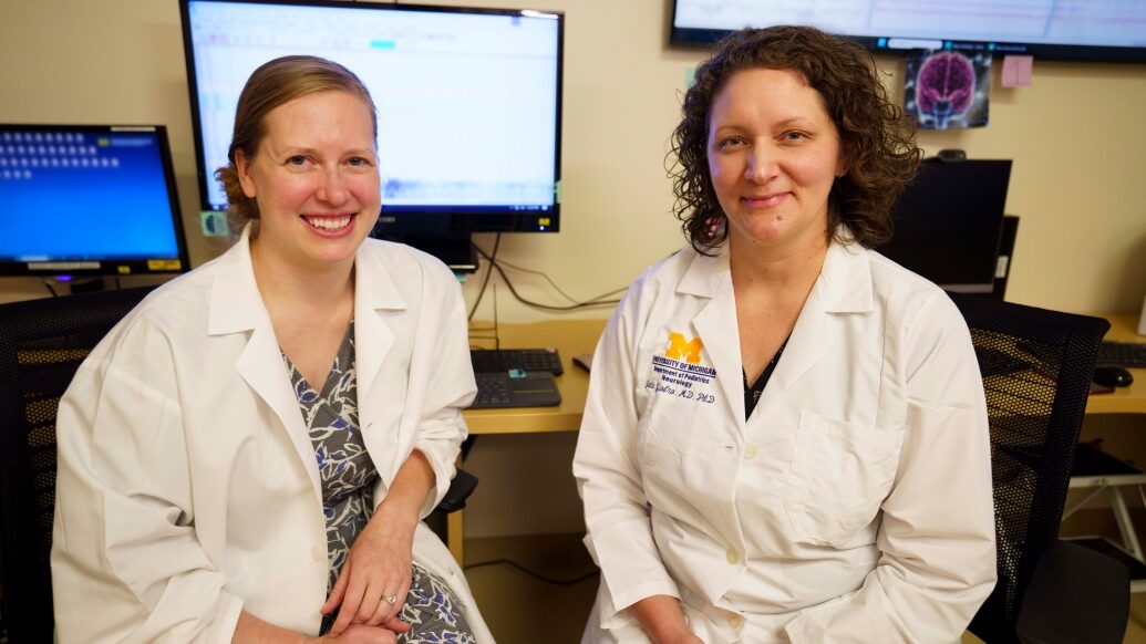 Doctors sitting together smiling at camera in office with computer in background