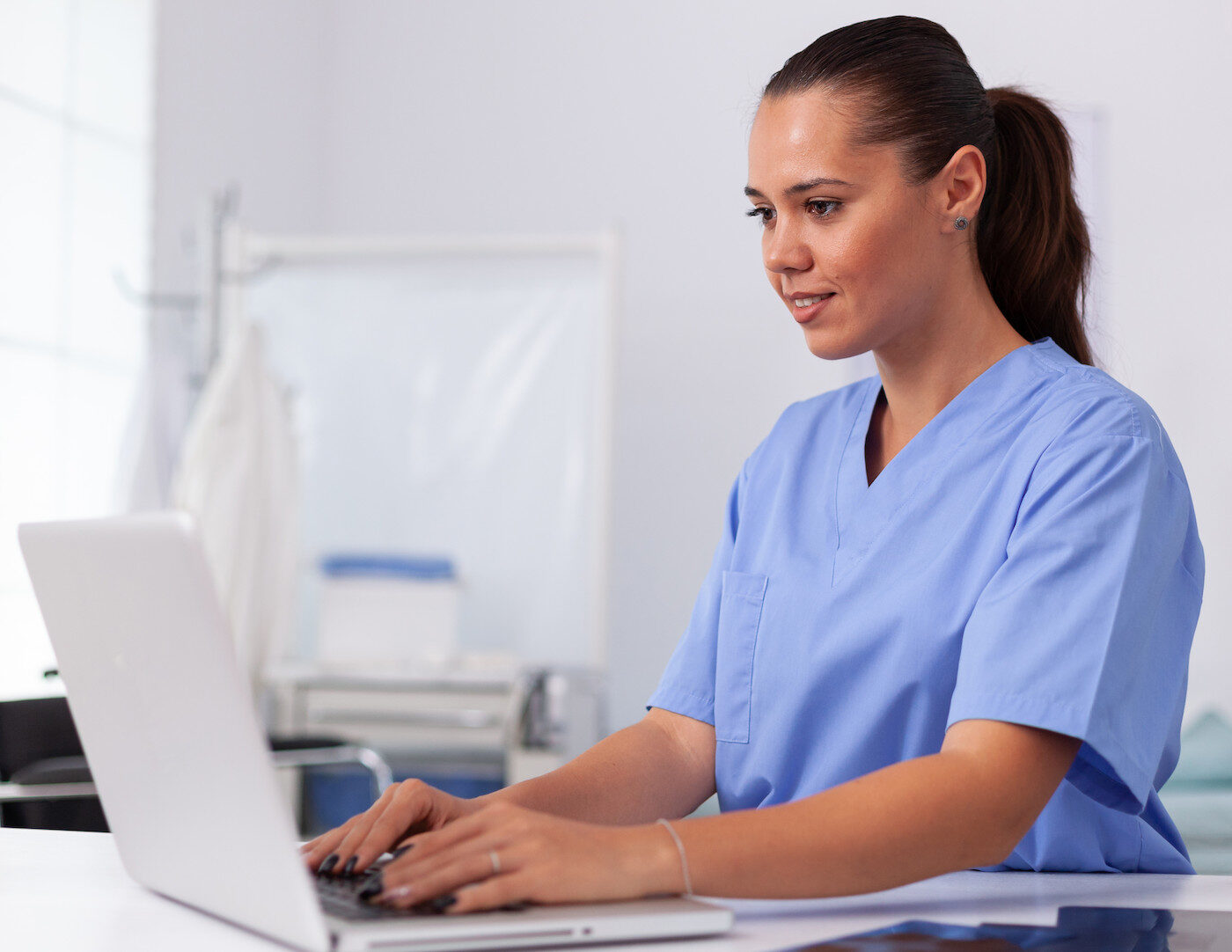 Woman in medical scrubs works on laptop computer