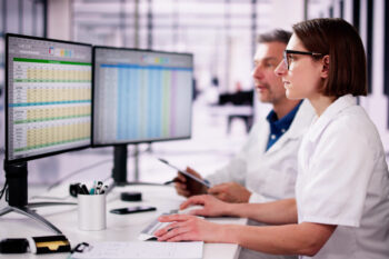 Two people sitting at a desk reviewing a budget spreadsheet on the computer
