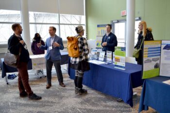Individuals standing around Medical School information table having a discussion during the 2025 Sustainable Lab Summit