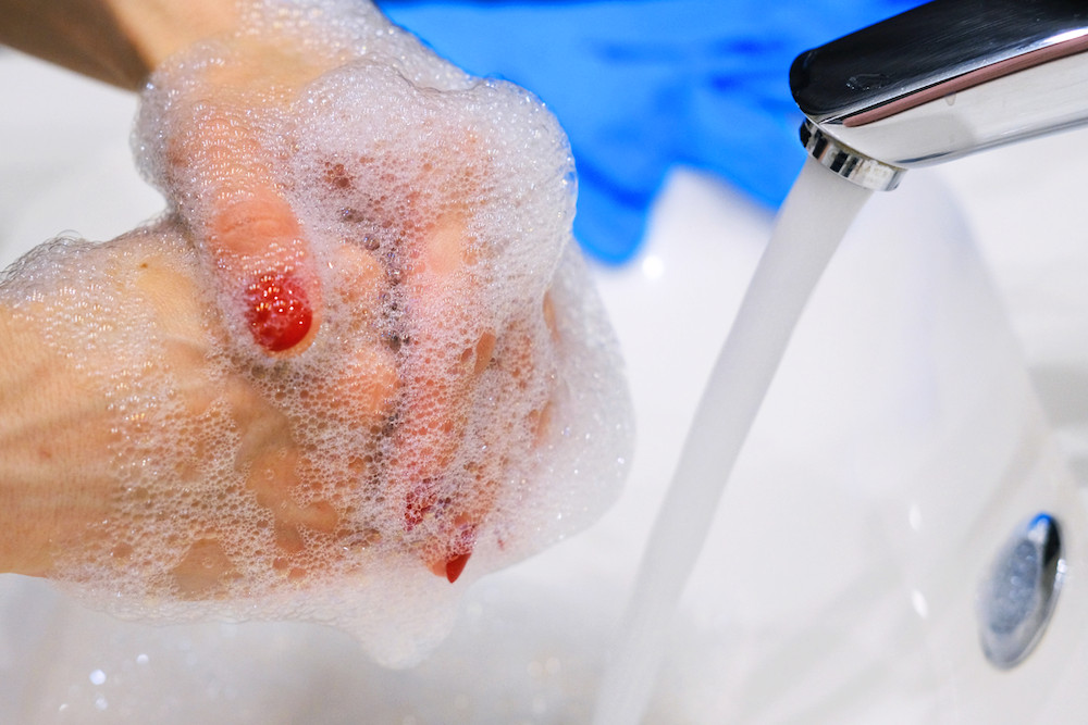 Close up of person washing hands in sink with disposable latex gloves in background