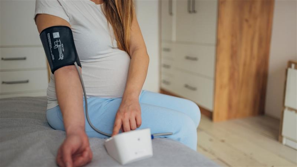 woman taking her blood pressure on bed while pregnant